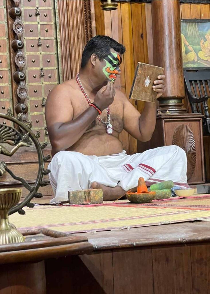 Un hombre pintándose la cara en un espectáculo de Kathakali en Kochi