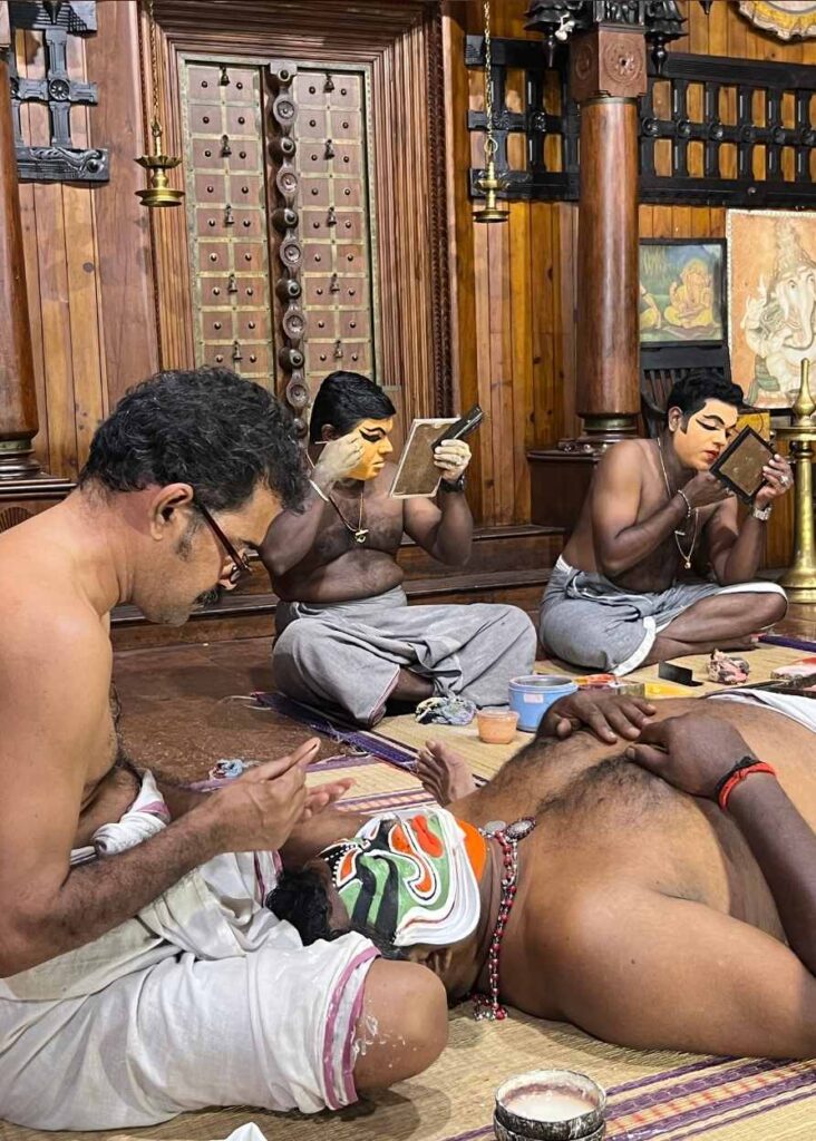 Un hombre pintándo la cara de otro hombre antes de un espectáculo de Kathakali en Kochi